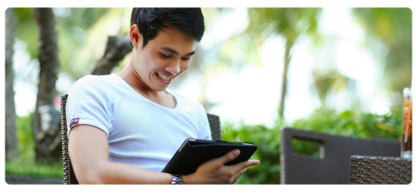 A young person with short dark hair smiles down at a tablet device